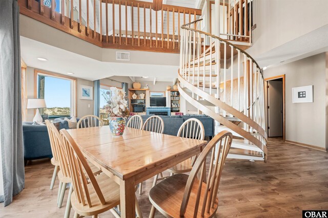 dining room featuring a high ceiling, wood finished floors, visible vents, baseboards, and stairway