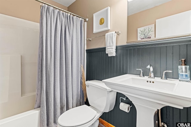 bathroom featuring a wainscoted wall, toilet, and shower / bath combo with shower curtain