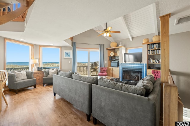 living area featuring lofted ceiling with beams, light wood-style flooring, a fireplace, a water view, and visible vents