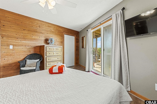 bedroom with wooden walls, ceiling fan, wood finished floors, access to outside, and a textured ceiling