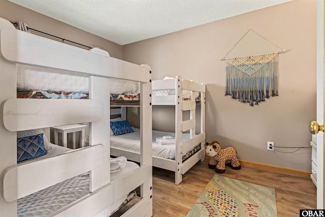 bedroom with light wood finished floors, baseboards, and a textured ceiling