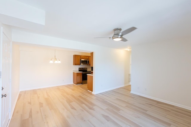 unfurnished living room with ceiling fan with notable chandelier, light wood-style flooring, and baseboards