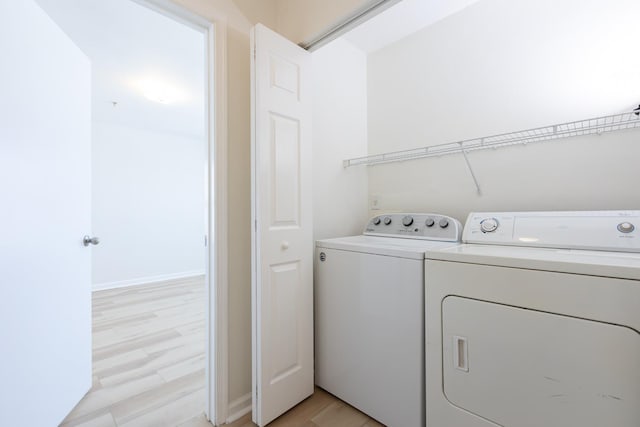 washroom with baseboards, laundry area, washer and clothes dryer, and light wood-style floors