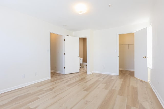 unfurnished bedroom with a spacious closet, a closet, light wood-style flooring, and baseboards