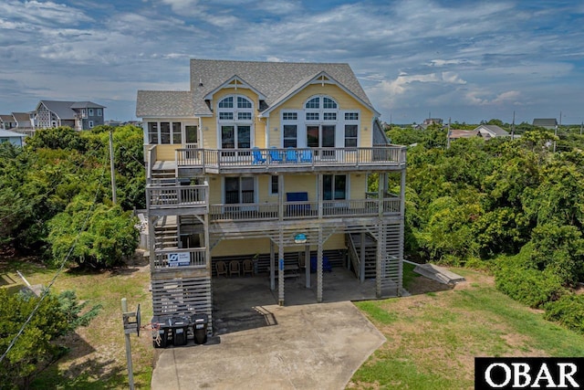 back of house featuring a carport, stairway, concrete driveway, and roof with shingles