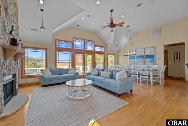 living room featuring light wood finished floors, visible vents, high vaulted ceiling, and a stone fireplace