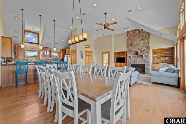 dining room featuring a stone fireplace, light wood finished floors, and high vaulted ceiling