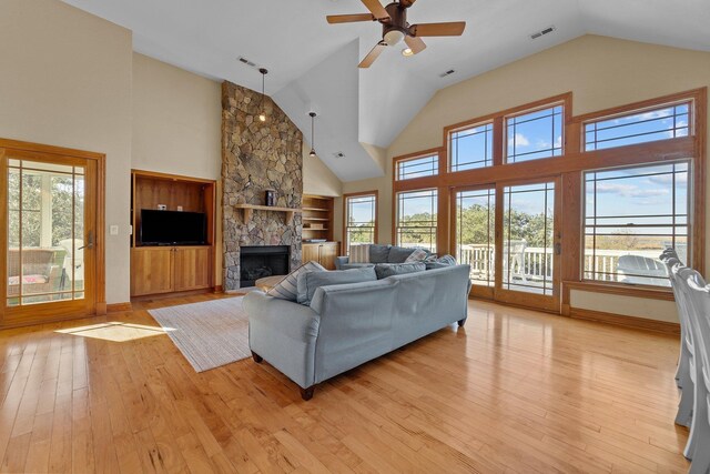 living room with light wood finished floors, visible vents, ceiling fan, a stone fireplace, and baseboards