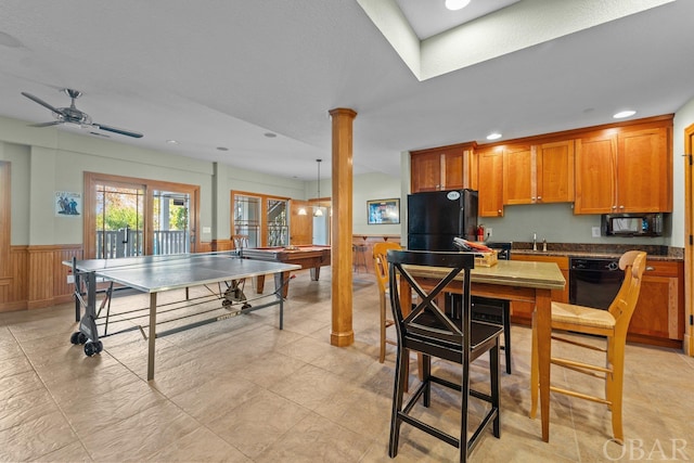 interior space with a wainscoted wall, black appliances, brown cabinetry, decorative columns, and pendant lighting