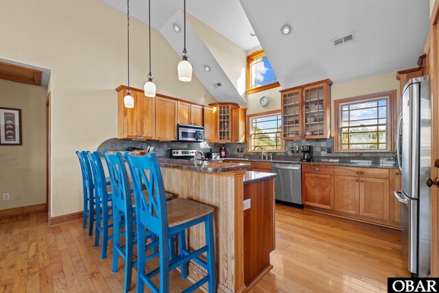 kitchen featuring visible vents, brown cabinetry, glass insert cabinets, appliances with stainless steel finishes, and a breakfast bar