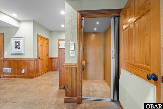 hall with wooden walls, visible vents, a wainscoted wall, elevator, and recessed lighting