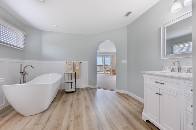 bathroom with a wainscoted wall, wood finished floors, vanity, visible vents, and a freestanding bath