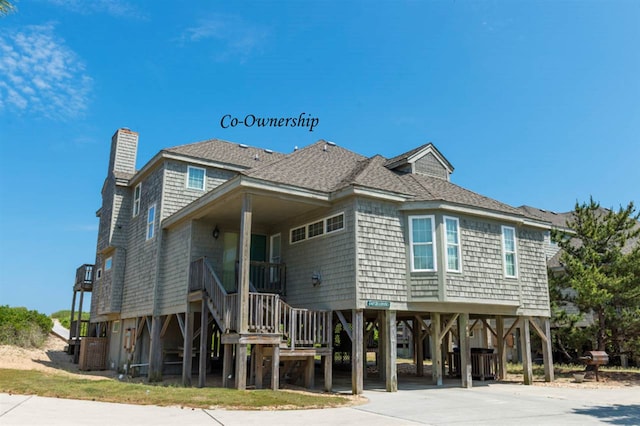 view of front facade with a carport, driveway, a shingled roof, and a chimney