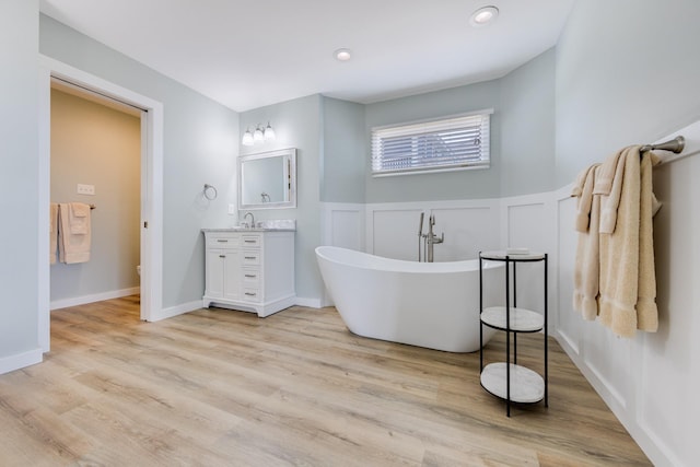 full bath with wainscoting, wood finished floors, vanity, a freestanding tub, and a decorative wall