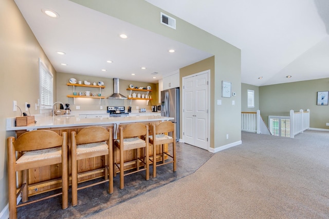 kitchen with a peninsula, visible vents, light countertops, wall chimney range hood, and open shelves