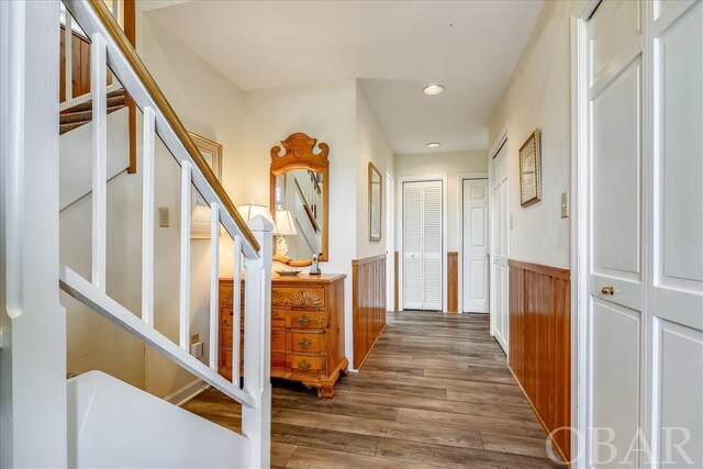 hall with a wainscoted wall, dark wood-type flooring, stairs, and recessed lighting