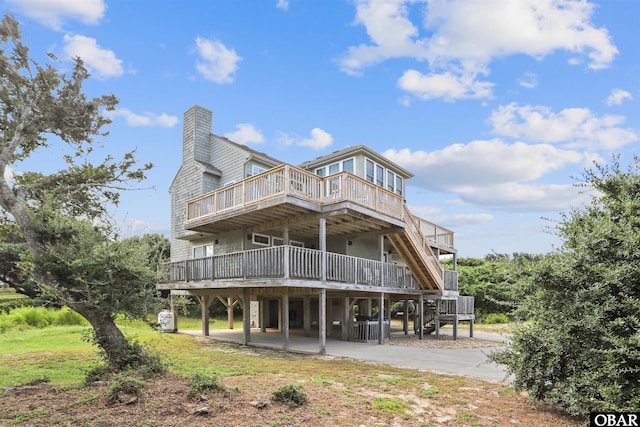 back of property featuring driveway, a chimney, a deck, and a patio