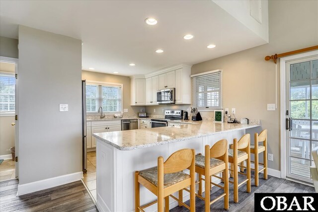 kitchen featuring a breakfast bar, a peninsula, light stone countertops, stainless steel appliances, and white cabinetry