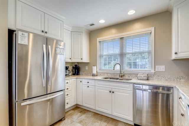 kitchen with white cabinets, light stone countertops, stainless steel appliances, and a sink