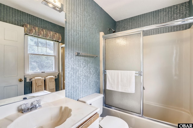 bathroom with shower / bath combination with glass door, vanity, toilet, and wallpapered walls