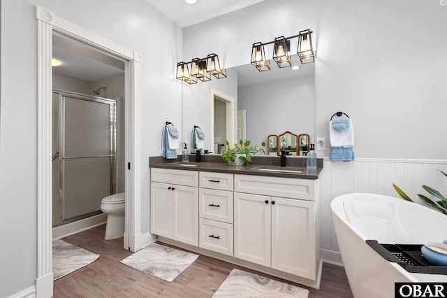 bathroom featuring a wainscoted wall, double vanity, a soaking tub, a shower stall, and wood finished floors