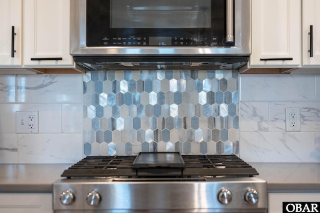 details with tasteful backsplash, stainless steel microwave, range, and white cabinetry