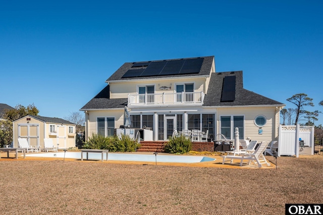 rear view of house featuring a patio, a balcony, solar panels, fence, and a storage unit