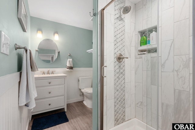 full bathroom with toilet, a wainscoted wall, wood finished floors, and a stall shower