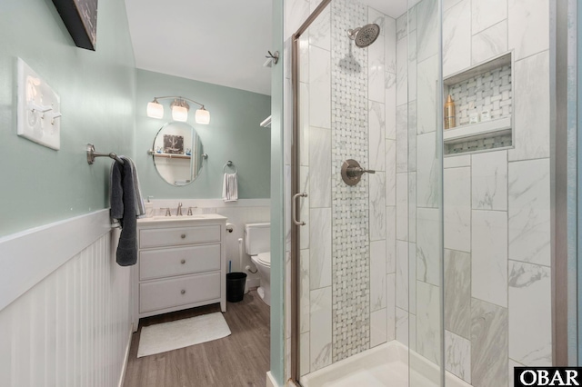 full bathroom featuring wainscoting, toilet, wood finished floors, vanity, and a shower stall