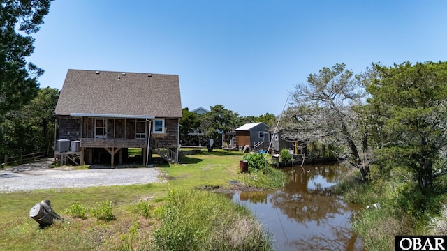 108 Loop Rd, Ocracoke, NC 27960 - rear view of house featuring stairs, roof with shingles, a water view, central AC unit, and a yard