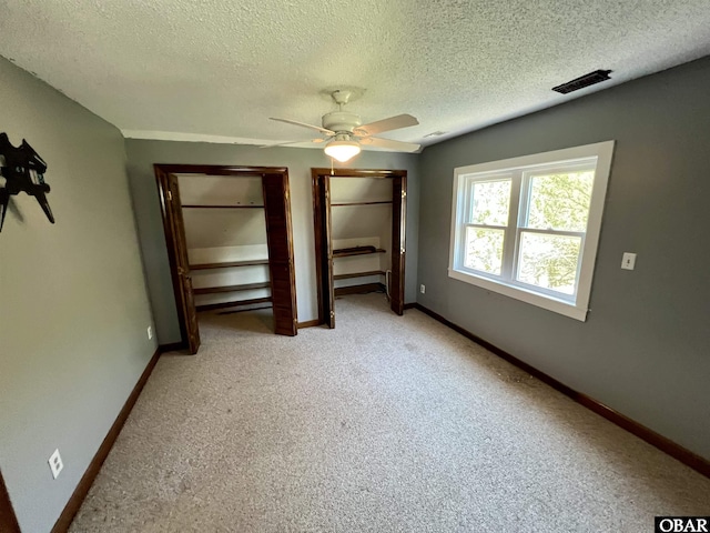 108 Loop Rd, Ocracoke, NC 27960 - unfurnished bedroom with light colored carpet, a textured ceiling, baseboards, a ceiling fan, and two closets