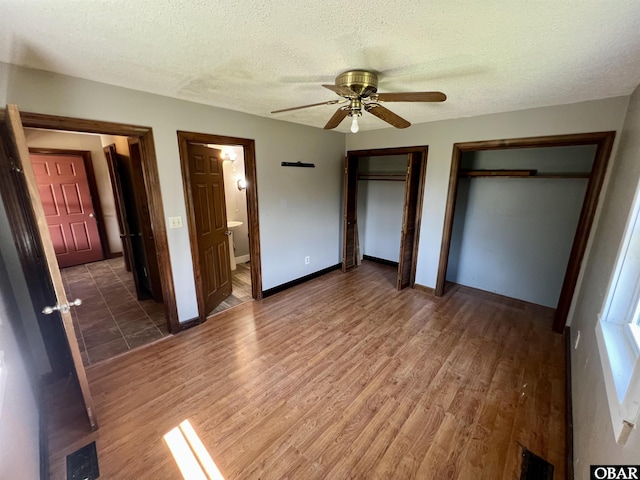 108 Loop Rd, Ocracoke, NC 27960 - unfurnished bedroom featuring a textured ceiling, two closets, light wood finished floors, a ceiling fan, and connected bathroom