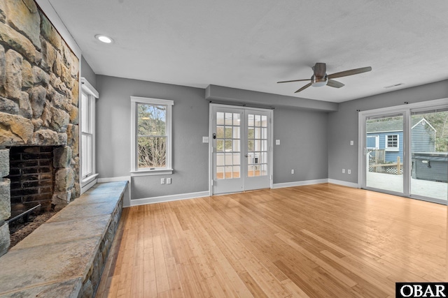 unfurnished living room featuring light wood-style floors, plenty of natural light, a fireplace, and french doors