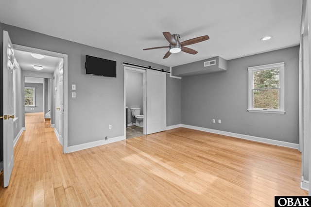 unfurnished bedroom featuring a barn door, connected bathroom, visible vents, baseboards, and light wood finished floors