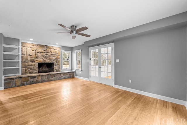 unfurnished living room with ceiling fan, a stone fireplace, light wood-style flooring, baseboards, and french doors