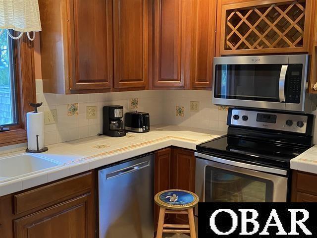 106 Middle Rd Lot 11, 12, Ocracoke, NC 27960 - kitchen featuring stainless steel appliances, backsplash, tile counters, and brown cabinets