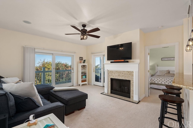 living area featuring light colored carpet, a fireplace with raised hearth, and ceiling fan