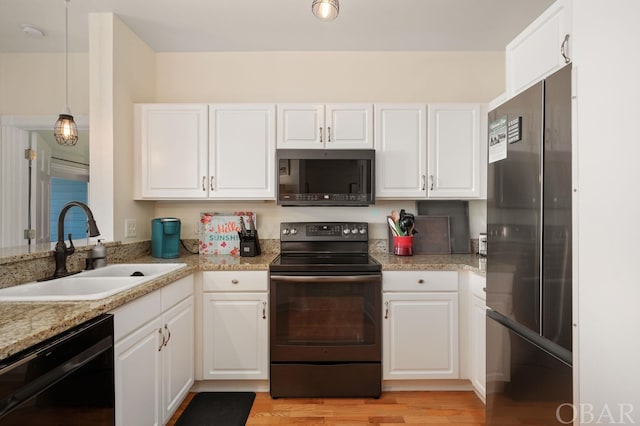 kitchen featuring a sink, white cabinetry, light wood-style floors, black appliances, and decorative light fixtures