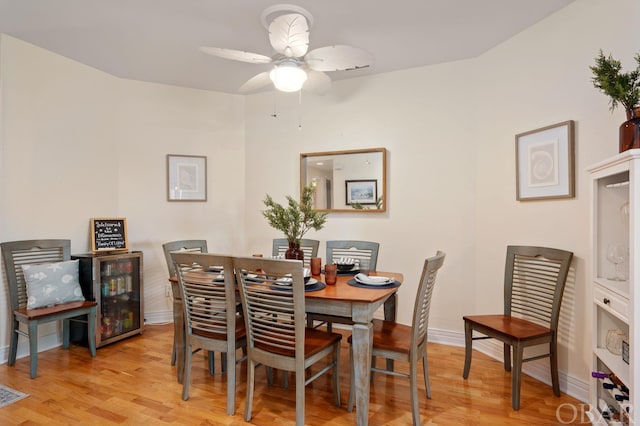 dining room with light wood-style floors, beverage cooler, ceiling fan, and baseboards