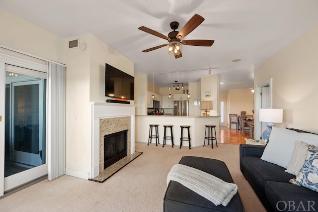 living room with light colored carpet, visible vents, rail lighting, a premium fireplace, and ceiling fan