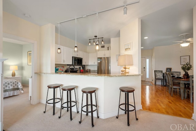 kitchen featuring a peninsula, a ceiling fan, white cabinets, freestanding refrigerator, and a kitchen bar