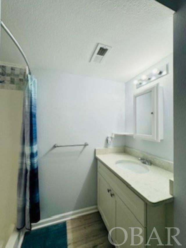 bathroom featuring a textured ceiling, wood finished floors, vanity, visible vents, and a stall shower