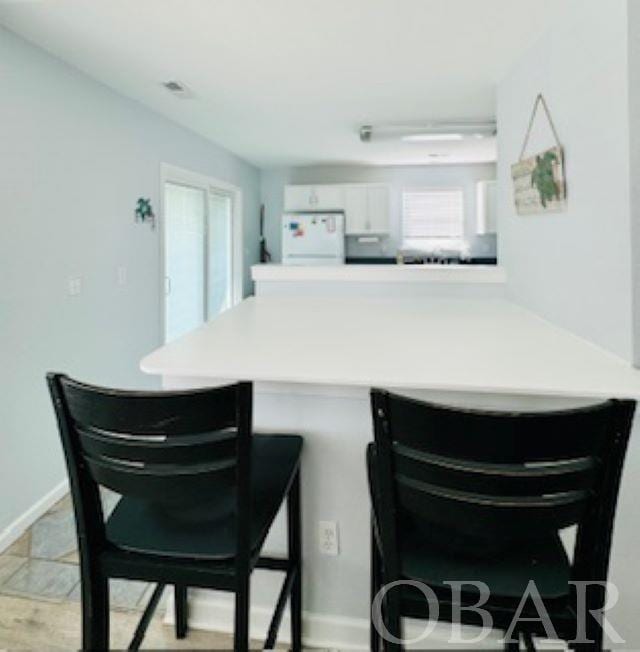 kitchen with a breakfast bar, light countertops, freestanding refrigerator, white cabinets, and a peninsula