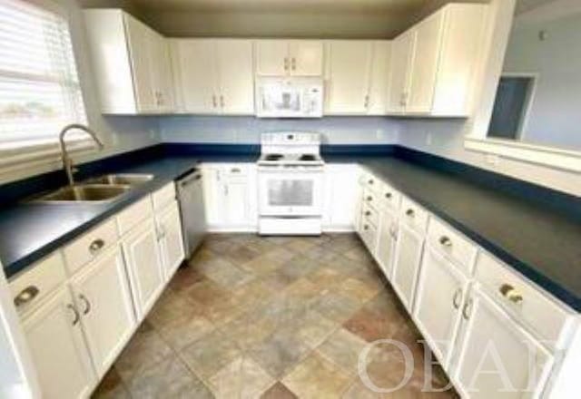 kitchen featuring dark countertops, white appliances, white cabinets, and a sink