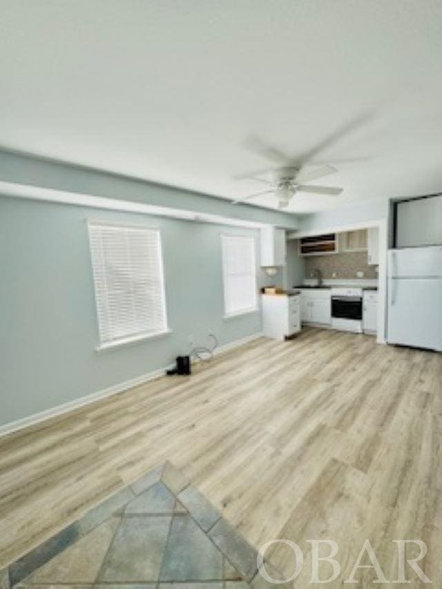 unfurnished living room featuring ceiling fan, light wood-type flooring, and baseboards