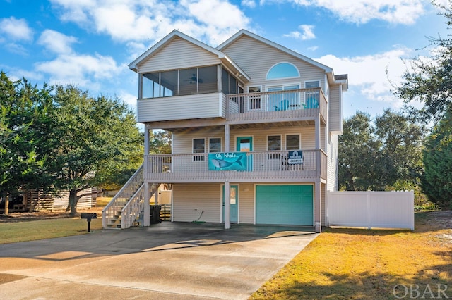 beach home featuring concrete driveway, a ceiling fan, a sunroom, a garage, and stairs