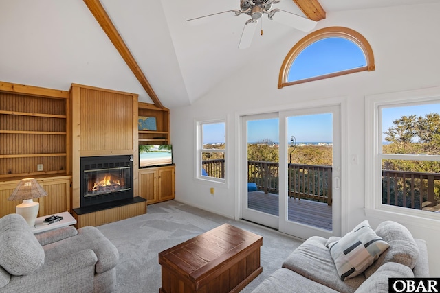 living area featuring beamed ceiling, high vaulted ceiling, a large fireplace, light colored carpet, and ceiling fan