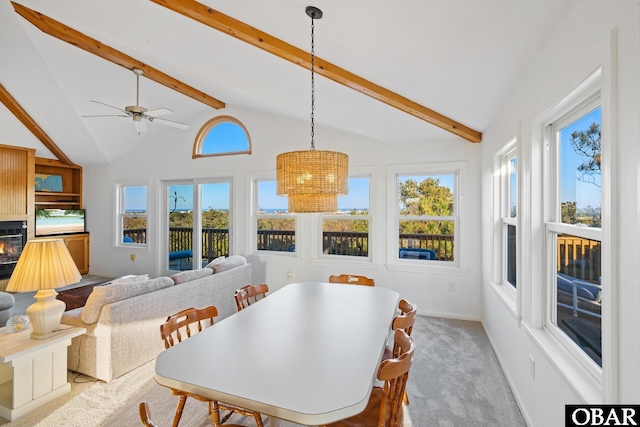 dining area featuring a glass covered fireplace, ceiling fan with notable chandelier, lofted ceiling with beams, and carpet floors