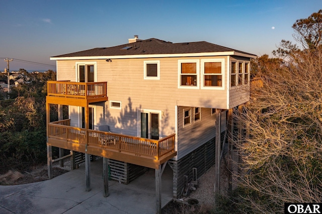 back of house at dusk featuring a carport, concrete driveway, and a balcony