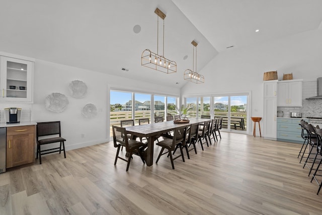 dining area with high vaulted ceiling, plenty of natural light, visible vents, and light wood-style floors